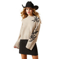 Woman wearing a beige sweater with floral designs and a black skirt on a white background