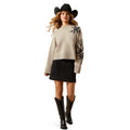 Woman wearing a beige sweater with floral embroidery, black skirt, and cowboy hat on a white background