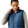 Woman wearing a blue puffer vest with a visible brand logo on a white background