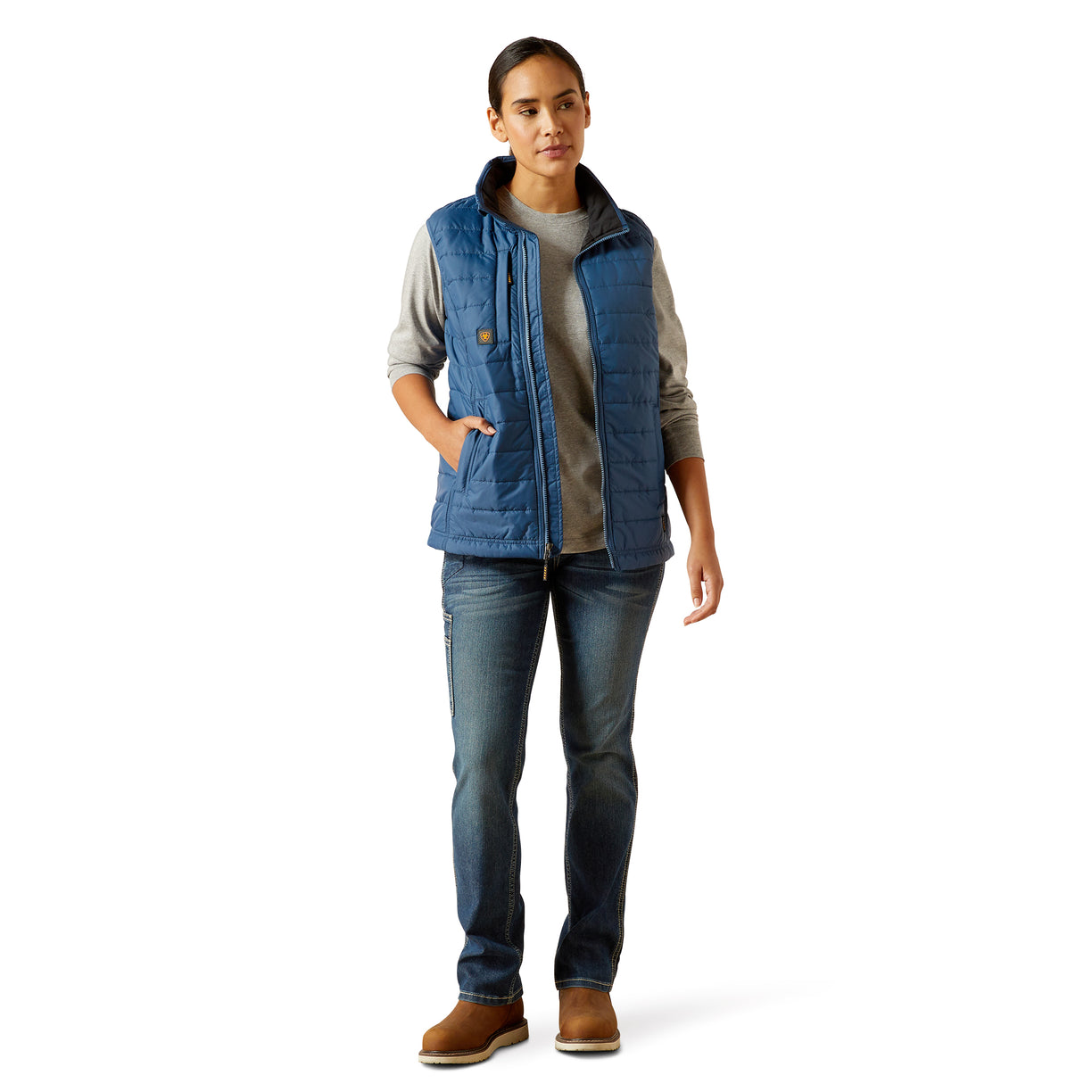 Woman wearing a blue vest over a gray shirt with jeans on a white background