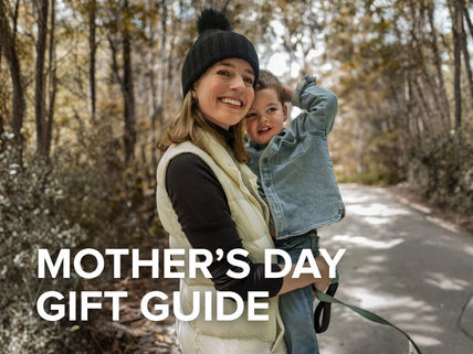 Woman holding a child in a forest with 'Mother's Day Gift Guide' text overlay
