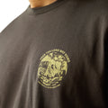 Man wearing a brown t-shirt with a scenic graphic on the back, standing against a white background