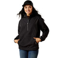 A woman wearing a black Ariat quarter-zip pullover jacket, blue jeans, and a black Ariat trucker hat, standing against a solid white background.