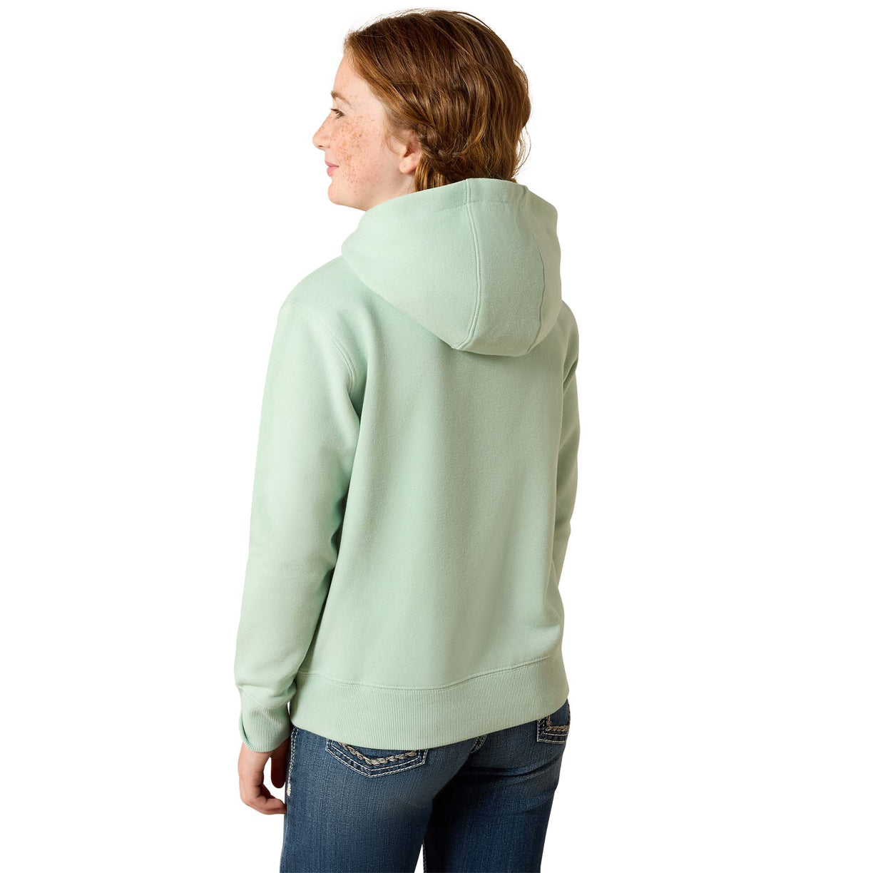 A woman with red hair is shown from the back wearing a light sage green pullover hoodie and blue jeans against a plain white background.