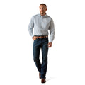 A man wearing a light blue and white patterned button-down shirt, dark blue jeans, and brown leather shoes, walking against a solid white background.