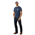 Man wearing a navy blue t-shirt with a logo, dark jeans, and brown boots against a beige background.