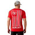 Man wearing a red Ariat t-shirt with a logo on the back against a beige background
