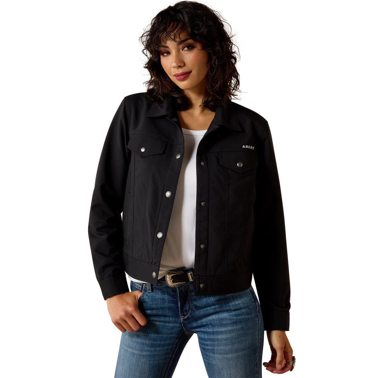 A woman modeling a black denim-style jacket with silver snap and button details, worn over a white top and blue jeans against a plain white background.
