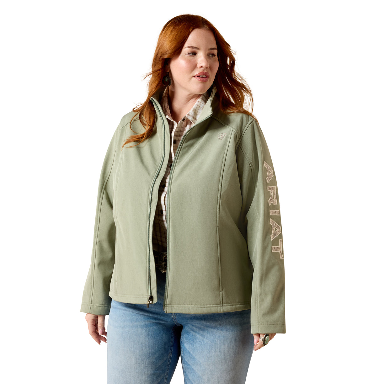 A woman modeling a sage green zip-up jacket with vertical 'AERAT' branding on the sleeve, paired with a patterned shirt and blue jeans against a white background.
