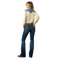 Woman wearing a cream long-sleeve shirt with denim accents and blue jeans on a white background