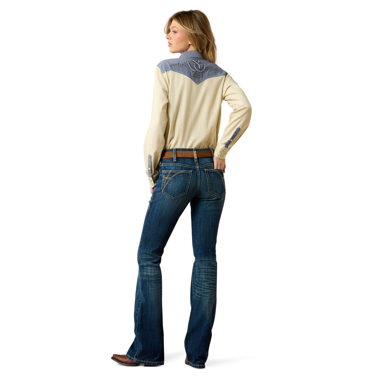 Woman wearing a cream long-sleeve shirt with denim accents and blue jeans on a white background