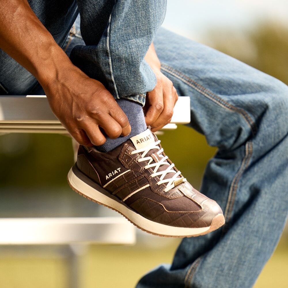Person tying brown sneakers on a blurred outdoor background