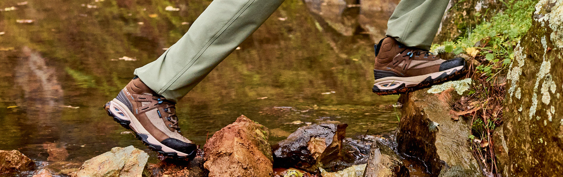 Woman hiker wearing new Ariat Traverse Hiking Boots and Pants crossing a creek.