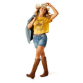 Woman wearing a yellow t-shirt, denim shorts, and brown cowboy boots on a white background