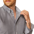 Man wearing a gray button-up shirt with rolled-up sleeves, adjusting the collar.