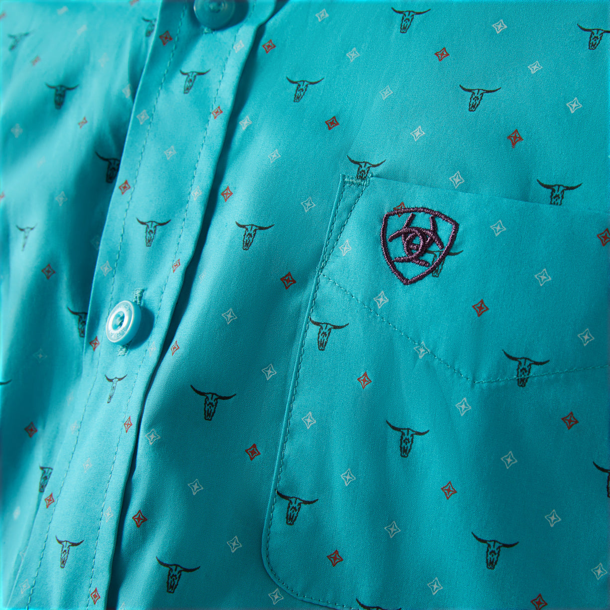 Close-up of a turquoise shirt with bull head pattern and embroidered logo.