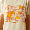 Beige t-shirt with a graphic of a cowboy on a horse, palm trees, and the word 'Ariat' on a beige background.