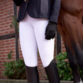 Person wearing white riding pants, black jacket, and brown boots standing next to a horse.