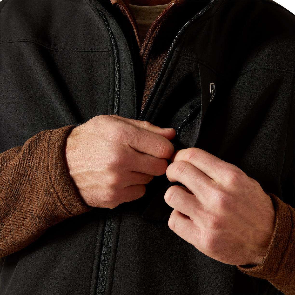 Person wearing a black jacket with a brand logo, adjusting the zipper.