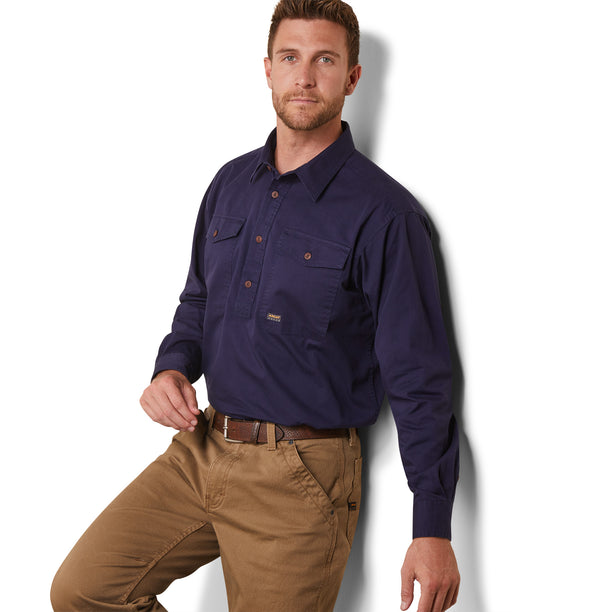 A man wearing a long sleeve navy blue workshirt with half buttons and large chest pockets, paired with light brown pants.